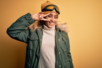 Young african american afro skier girl wearing snow sportswear and ski goggles Doing peace symbol with fingers over face, smiling cheerful showing victory