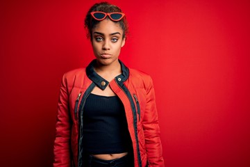 Beautiful african american girl wearing red jacket and sunglasses over isolated background depressed and worry for distress, crying angry and afraid. Sad expression.