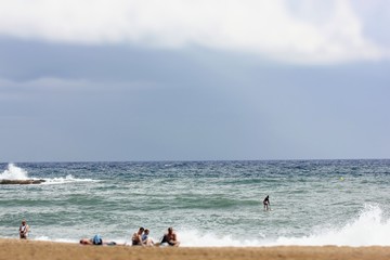 Surfer catches a wave on a board in the sea and the company of people resting on the beach in the summer holidays.