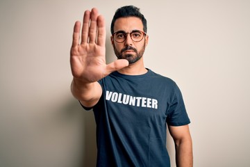 Handsome man with beard wearing t-shirt with volunteer message over white background doing stop...