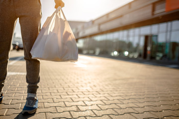 Obraz premium Close-up, a plastic bag filled with groceries, food vegetables and fruits, dairy products. A man stands in parking near a shopping center or a shopping mall. He bought everything at the supermarket