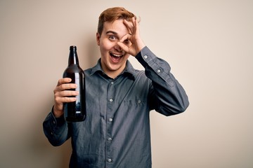 Young handsome redhead man drinking bottle of beer over isolated white background smiling happy doing ok sign with hand on eye looking through fingers