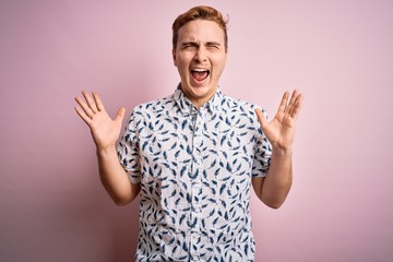 Naklejka premium Young handsome redhead man wearing casual summer shirt standing over pink background celebrating mad and crazy for success with arms raised and closed eyes screaming excited. Winner concept