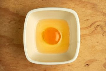 huevo crudo vaciado en un plato blanco cuadrado sobre superficie de madera
