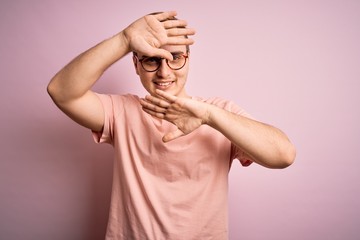 Young handsome redhead man wearing casual t-shirt standing over isolated pink background Smiling cheerful playing peek a boo with hands showing face. Surprised and exited