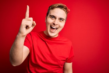 Naklejka premium Young handsome redhead man wearing casual t-shirt over isolated red background pointing finger up with successful idea. Exited and happy. Number one.
