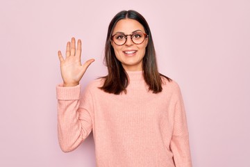 Young beautiful brunette woman wearing casual sweater and glasses over pink background showing and pointing up with fingers number five while smiling confident and happy.