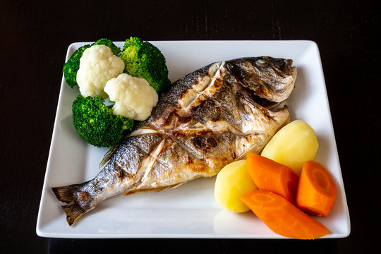 Mediterranean sea dish, Sparus aurata of baked fish vegetables and boiled potatoes on a black background. Healthy food.