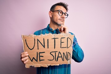 Young handsome activist man asking for union holding banner with united stand message serious face thinking about question, very confused idea