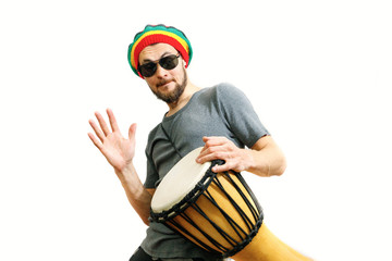 Young caucasian smiling man in rasta hat, sunglasses and grey t-shirt on white background play on...