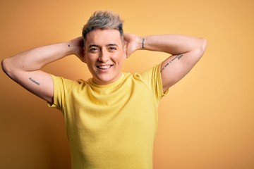 Young handsome modern man wearing yellow shirt over yellow isolated background relaxing and stretching, arms and hands behind head and neck smiling happy