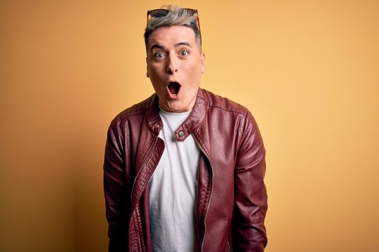 Young handsome modern man wearing fashion leather jacket and sunglasses over yellow background afraid and shocked with surprise expression, fear and excited face.
