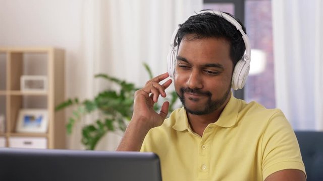 remote job, technology and people concept - happy smiling young indian man in headphones with laptop computer working at home office