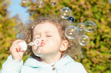 portrait little cute girl blows soap bubbles. happy child plays outside. baby plays outdoors in nature.