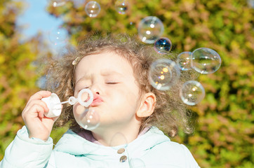 portrait little cute girl blows soap bubbles. happy child plays outside. baby plays outdoors in...