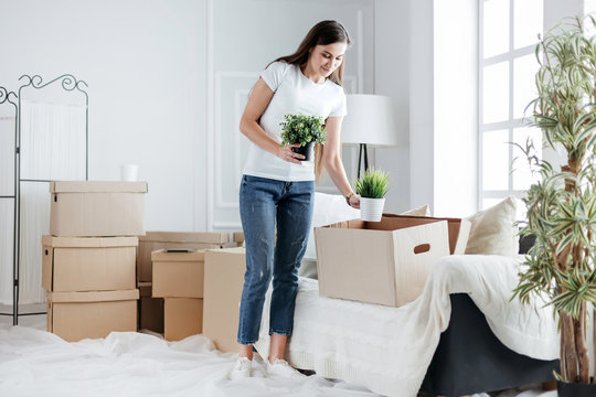 young woman takes her favorite plants out of a cardboard box