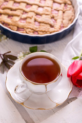 White porcelain cup of tea, and fresh-baked pie. English breakfast still-life with drink and treats red tulip flower and white tablecloth.