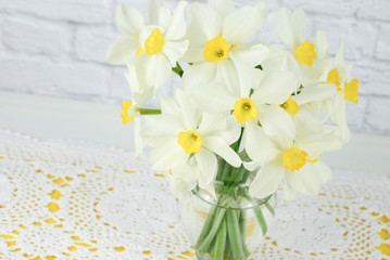 Vase of white and yellow daffodil flowers with white lace doily as background