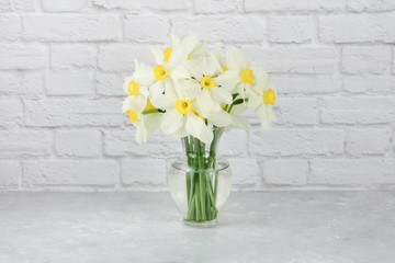Vase of white and yellow daffodil flowers displayed on a granite counter with a white brick wall background