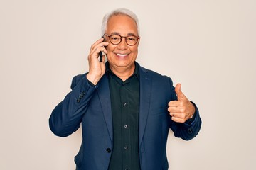 Middle age senior grey-haired business man wearing glasses talking on smartphone happy with big smile doing ok sign, thumb up with fingers, excellent sign