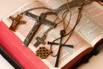 A group of Christian crosses  worn by a pastor displayed on a red-letter edition of the Bible.