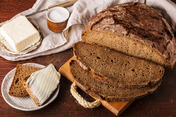 Freshly baked rye bread on wooden board, cotton napkin. Brown background, horizontal format