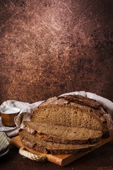 Freshly baked rye bread on wooden board, cotton napkin. Brown background, vertical format