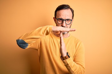 Middle age hoary man wearing casual sweater and glasses over isolated yellow background Doing time out gesture with hands, frustrated and serious face
