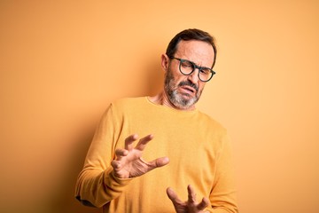 Obraz premium Middle age hoary man wearing casual sweater and glasses over isolated yellow background disgusted expression, displeased and fearful doing disgust face because aversion reaction.