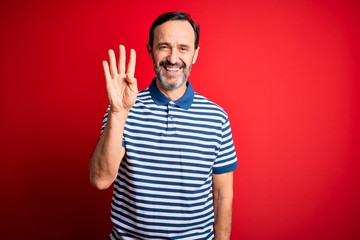 Naklejka premium Middle age hoary man wearing casual striped polo standing over isolated red background showing and pointing up with fingers number four while smiling confident and happy.