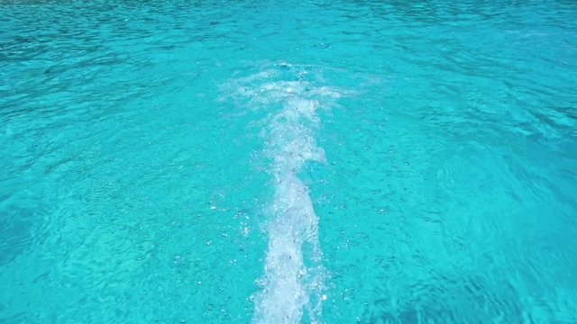 Jet of water and air flowing into a sparkling clean blue swimming pool moving away from the camera in close up causing turbulence. Slow motion