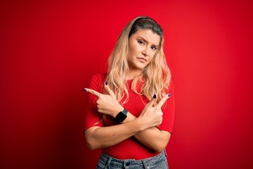 Young beautiful blonde woman wearing casual t-shirt standing over isolated red background Pointing to both sides with fingers, different direction disagree