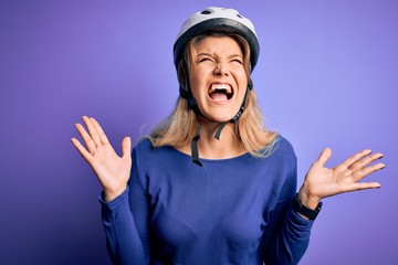 Young beautiful blonde cyclist woman wearing bike security helmet over purple background celebrating mad and crazy for success with arms raised and closed eyes screaming excited. Winner concept