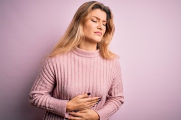 Naklejka premium Young beautiful blonde woman wearing casual pink sweater over isolated background with hand on stomach because indigestion, painful illness feeling unwell. Ache concept.