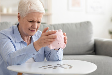 Financial Crisis. Sad Senior Woman Shaking Piggy Bank, Taking Out Coins