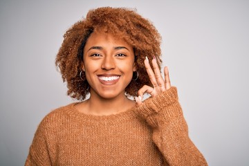 Young beautiful African American afro woman with curly hair wearing casual sweater doing ok sign with fingers, excellent symbol