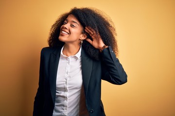 Young beautiful african american business woman with afro hair wearing elegant jacket smiling with hand over ear listening an hearing to rumor or gossip. Deafness concept.