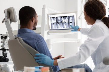 Female dentist and male patient watching xray on digital screen