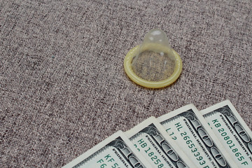 Unpacked condom and a lot of notes for $ 100 on the background of the sofa, toned