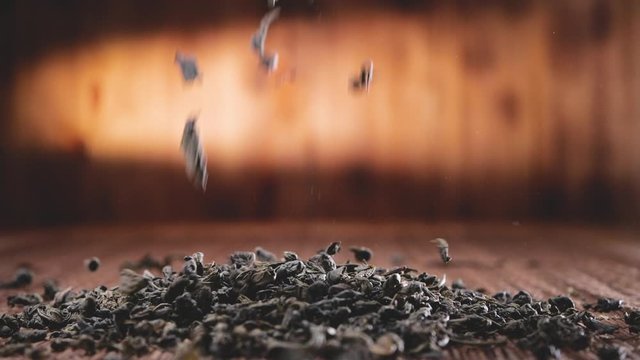 Falling tea leaves on wooden background, in slow motion
