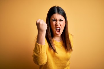 Young beautiful woman wearing casual sweater over yellow isolated background angry and mad raising...
