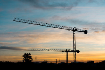 Silhouettes of tower cranes against the night sky House under construction. Industrial corner