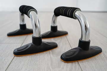 close up on metal shiny push up bars with black handle and base training equipment on the wooden floor at home in day