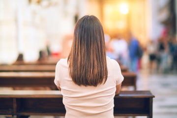 Young beautiful woman praying on her knees in a bench at church