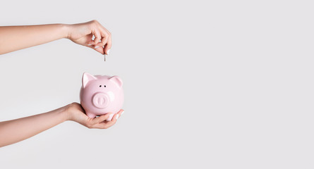 Saving money. Female hand putting coin into piggy bank on light background, closeup. Copy space....