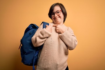 Obraz premium Young down syndrome student woman wearing school bag over yellow background very happy pointing with hand and finger