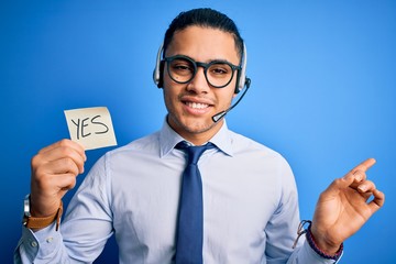 Young brazilian call center agent man holding reminder paper with yes message very happy pointing...