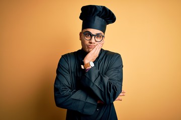 Young brazilian chef man wearing cooker uniform and hat over isolated yellow background thinking looking tired and bored with depression problems with crossed arms.