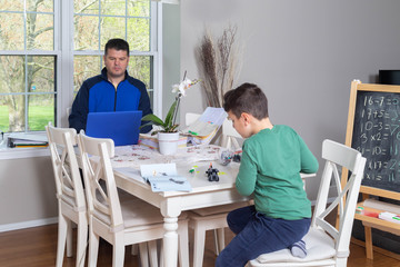 Father working from home while his child is playing in the dining  table