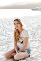 Portrait of young pretty woman sitting on the beach and looking at the camera